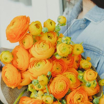Crop female florist browsing smartphone while standing with bunch of yellow flowers